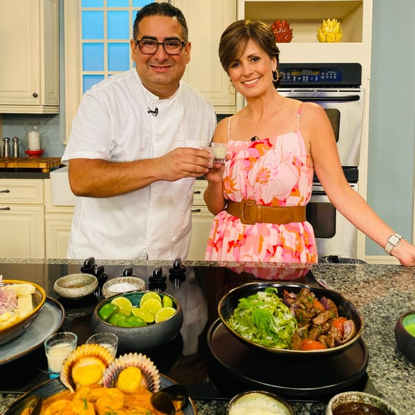 A chef and woman toast with small drinks over a counter with Peruvian dishes like ceviche and lomo saltado.