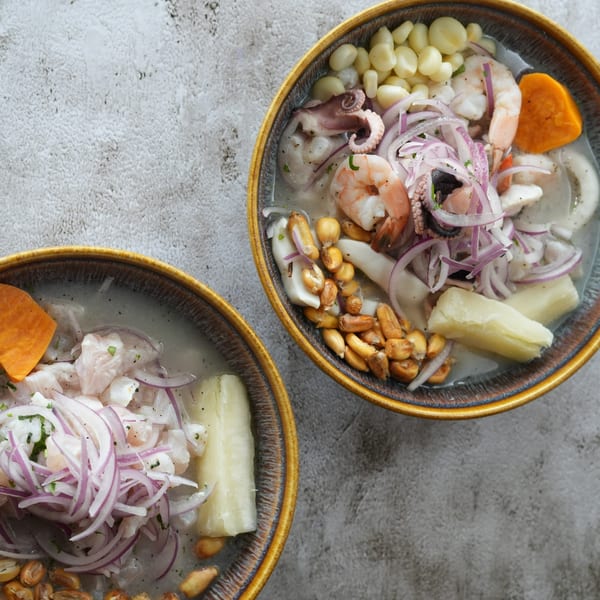 Two bowls of Peruvian ceviche with seafood, corn, sweet potato, and red onion.
