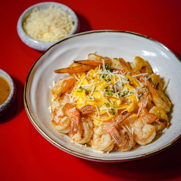 Peruvian shrimp fettuccine with yellow sauce, grated cheese, and parsley on a red background.