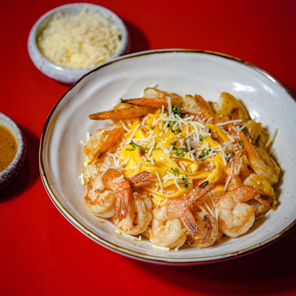 Peruvian shrimp fettuccine with yellow sauce, grated cheese, and parsley on a red background.