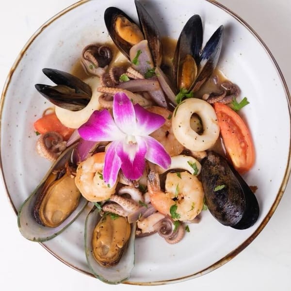Peruvian seafood dish with mussels, shrimp, calamari, octopus, and vegetables, garnished with an orchid.