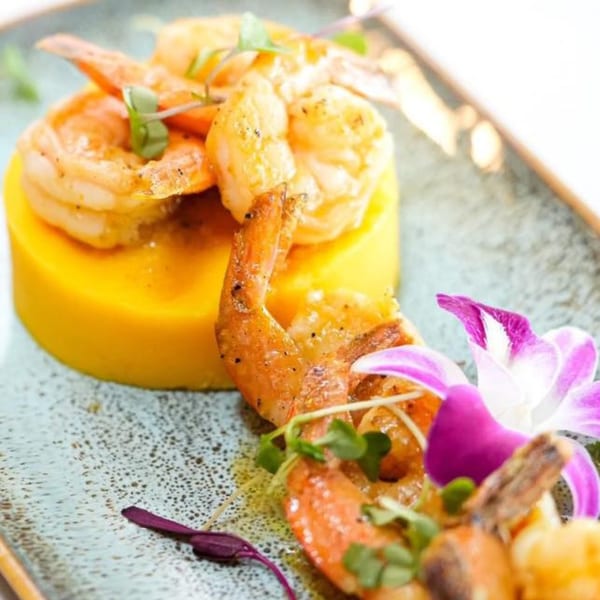 Peruvian grilled shrimp with yellow mashed potatoes, garnished with microgreens and an orchid.
