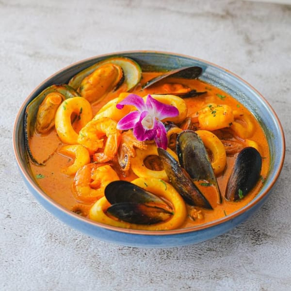 Peruvian seafood stew with mussels, shrimp, and calamari in a rich orange broth, garnished with an orchid.