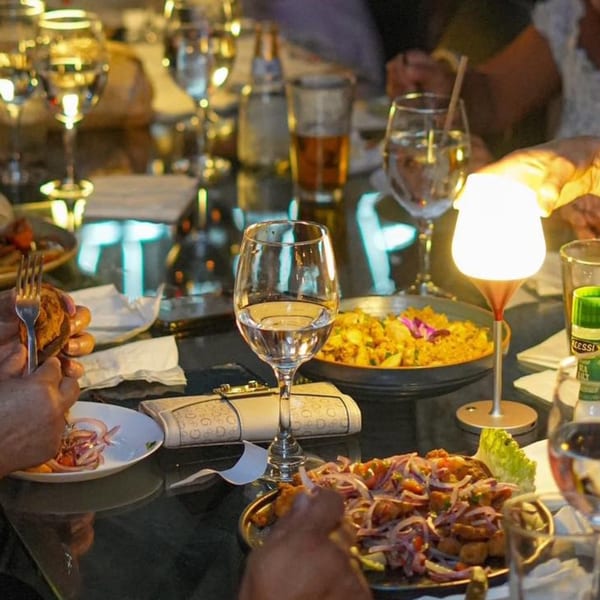 Diners enjoying Peruvian dishes and drinks at a restaurant table with a glowing lamp.