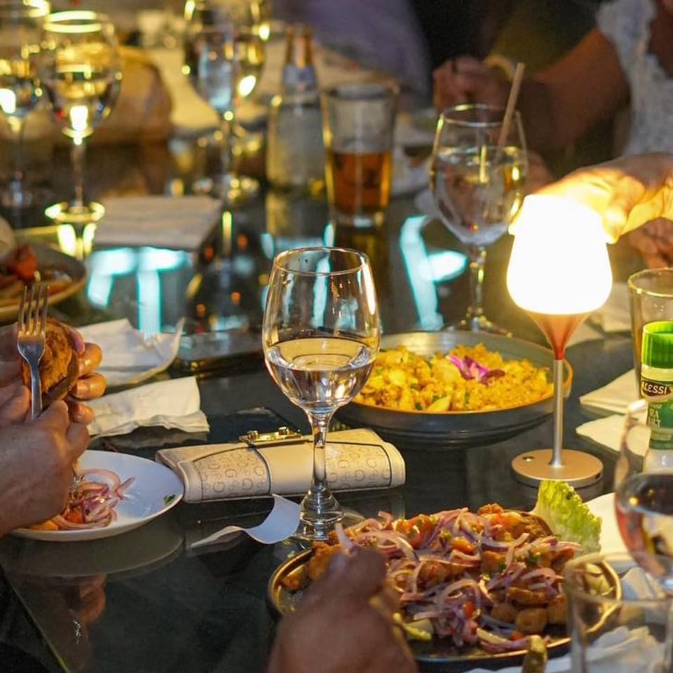 Diners enjoying Peruvian dishes and drinks at a restaurant table with a glowing lamp.