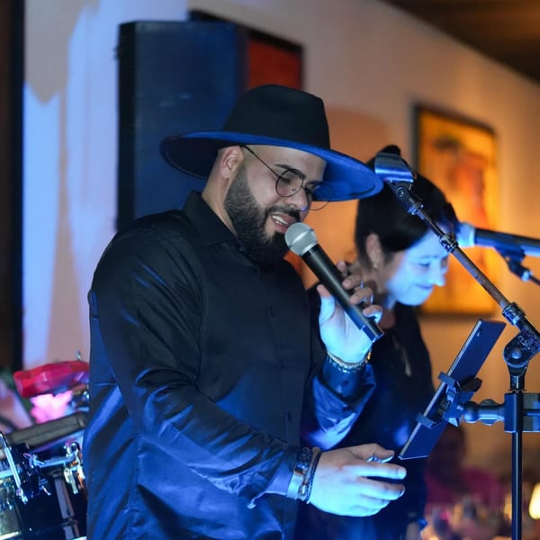 A man in a black hat and shirt sings into a microphone at Costanera Peruvian Cuisine.