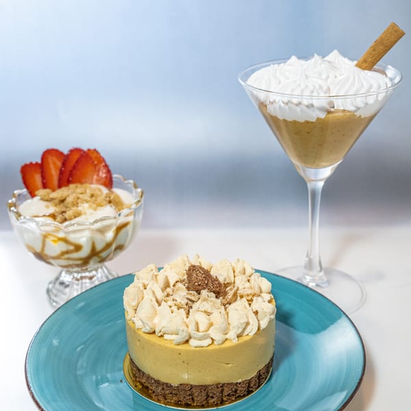 Three Peruvian desserts: a cheesecake, a parfait with strawberries, and a creamy drink with a cinnamon stick.