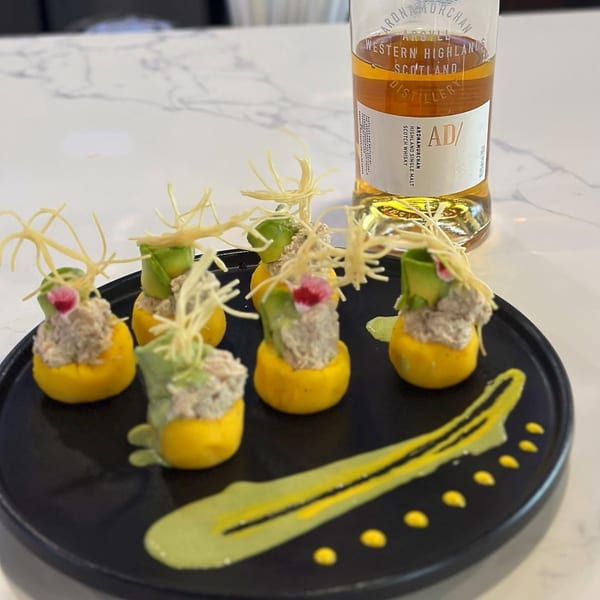 Peruvian causa rellena appetizers with avocado, tuna, and crispy garnish, next to a bottle of Scotch whisky.