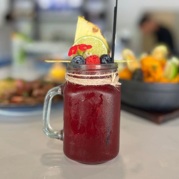 A Peruvian chicha morada drink in a mason jar, garnished with pineapple, lime, berries, and flowers.