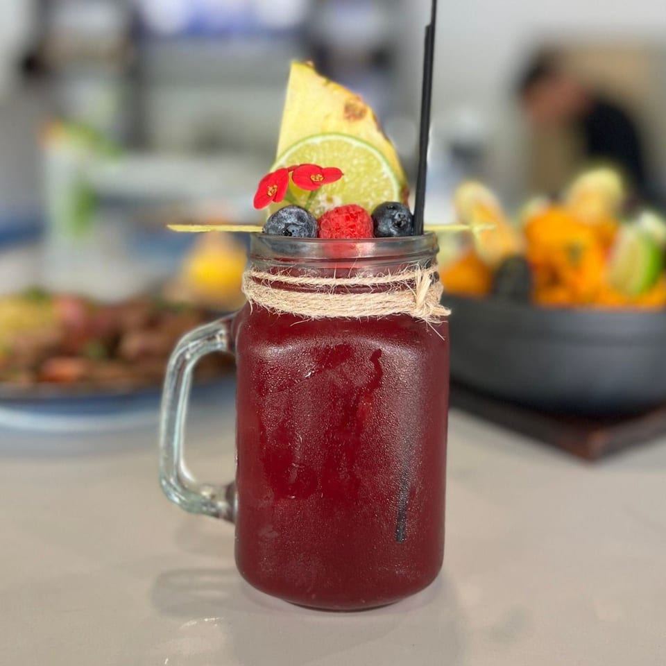 A Peruvian chicha morada drink in a mason jar, garnished with pineapple, lime, berries, and flowers.