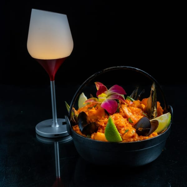 Peruvian seafood paella with mussels, lime, and an orchid, next to a glowing wine glass.