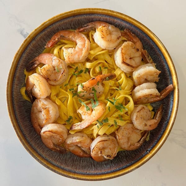 Peruvian shrimp fettuccine with parsley in a rustic bowl on a white marble surface.