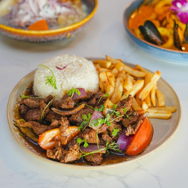 Peruvian Lomo Saltado with beef, onions, tomatoes, rice, and fries on a plate.