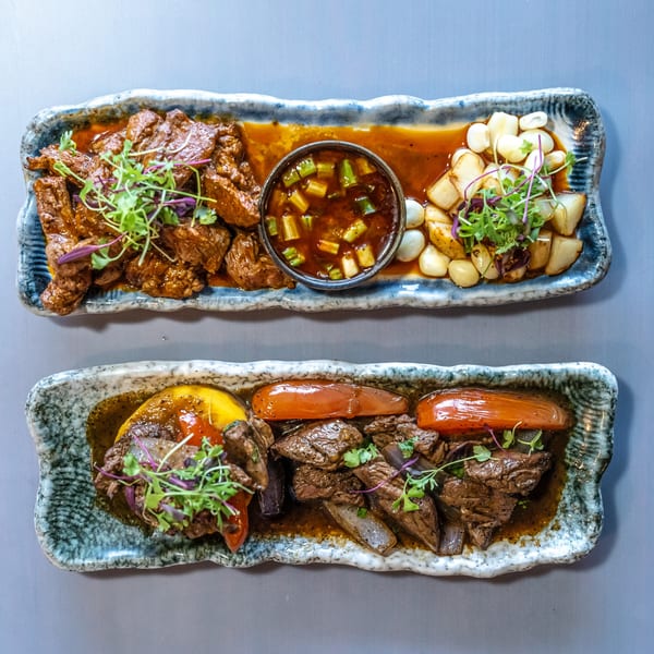 Two rectangular plates of Peruvian beef stew, one with corn and potatoes, the other with peppers.