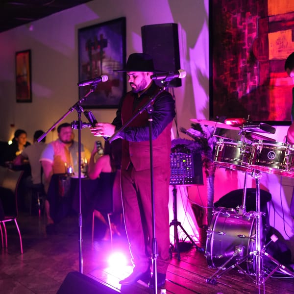 Musicians performing live on stage with drums and microphones under purple lighting at Costanera Peruvian Cuisine.